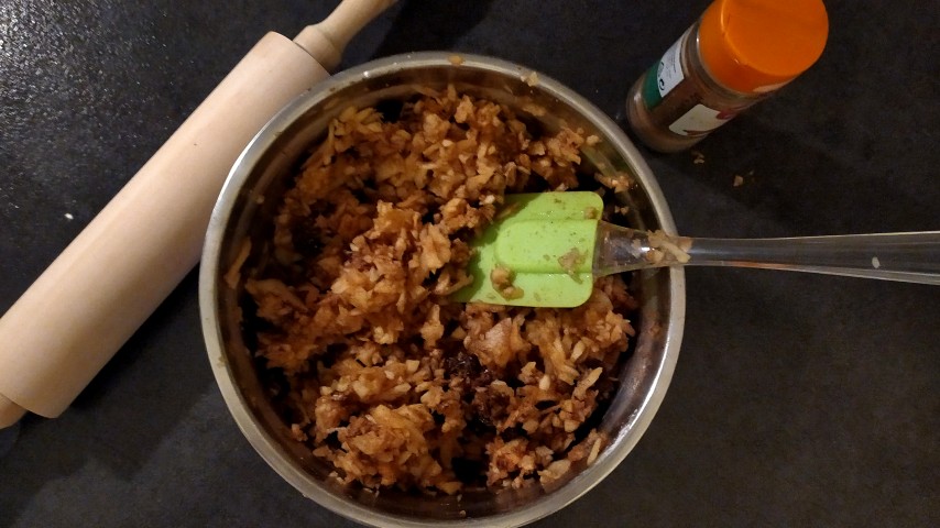 Μπολ με τη γέμιση μήλου με μια σπάτουλα μέσα, πλάστης και βαζάκι με κανέλα σε πάγκο κουζίνας