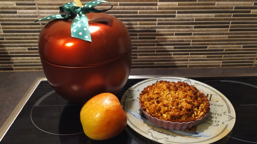 Μια ατομική τάρτα μήλου σε πιάτο, ένα μήλο και ένα μεγάλο διακοσμητικό κόκκινο κουτί σε σχήμα μήλο στην κουζίνα