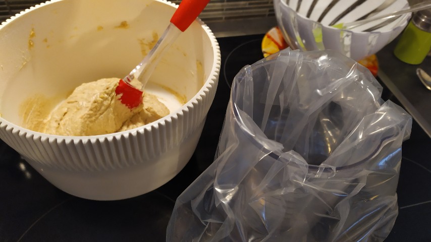 Μπωλ με την έτοιμη ζύμη και μια σπάτουλα σιλικόνης και δίπλα ένα δοχείο με μια σακούλα τροφίμων μέσα