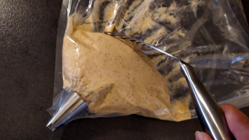 Η σακούλα γεμισμένη με τη ζύμη, στον πάγκο και μια μεταλλική σπάτουλα που σπρώχνει τη ζύμη προς τα κάτω